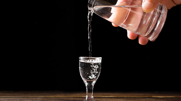 Someone pouring a shot of clear spirit into a small glass.