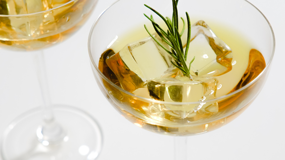 A coupe glass with a light-coloured cocktail with the tip of rosemary resting in the middle